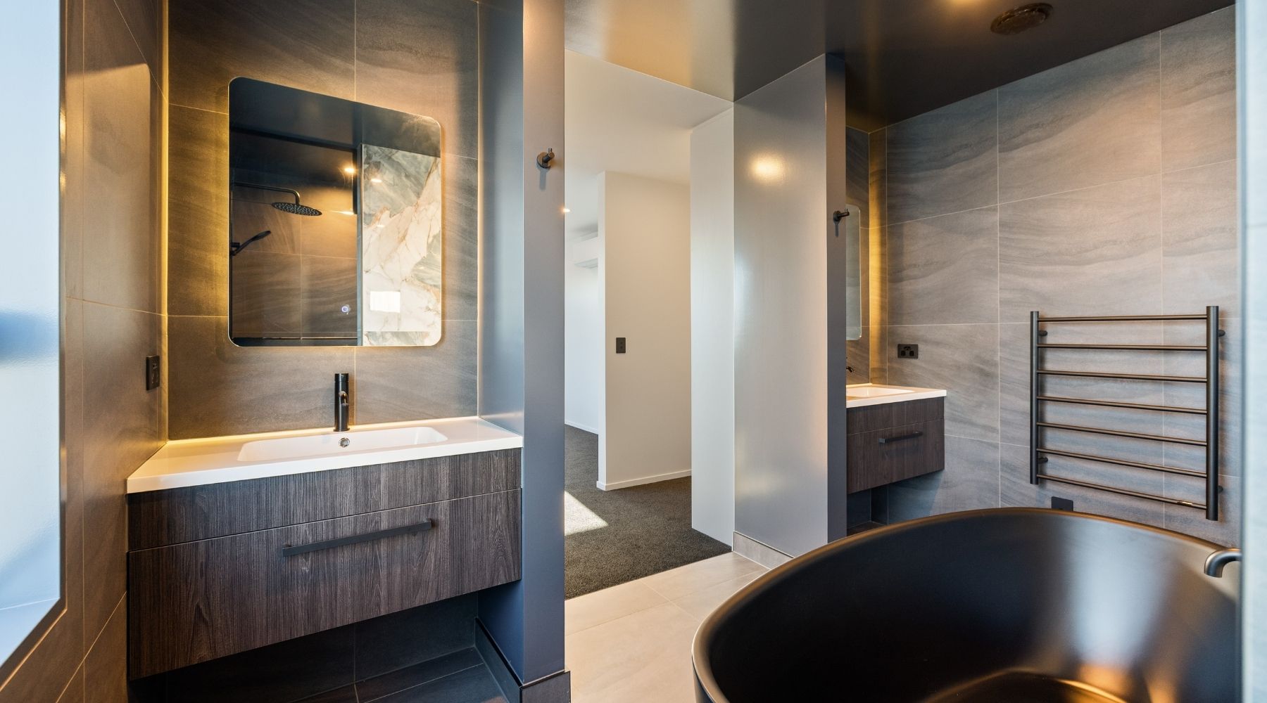 Contemporary ensuite by Hallmark Homes, featuring dark tile, matte black fixtures, and a standout marble wall design.