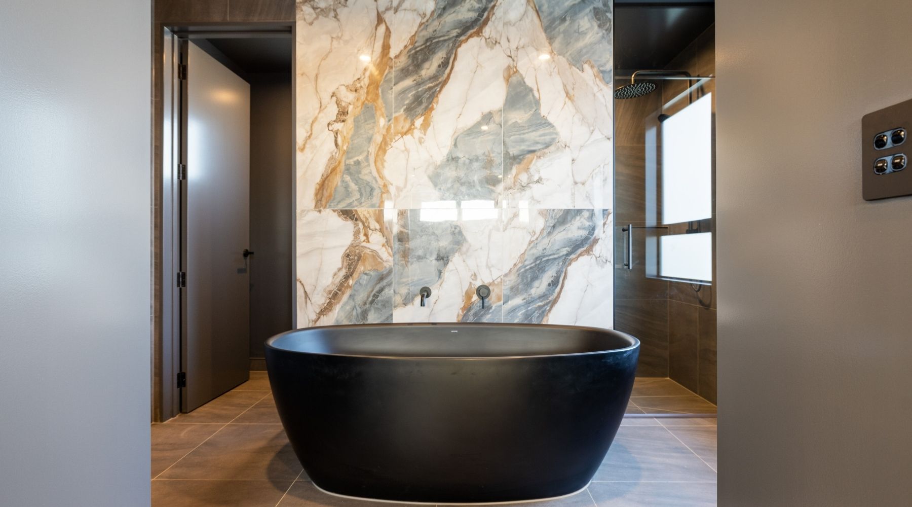 Luxury ensuite design from Hallmark Homes — black bath, marble accent wall, and moody ceiling in a Christchurch build.