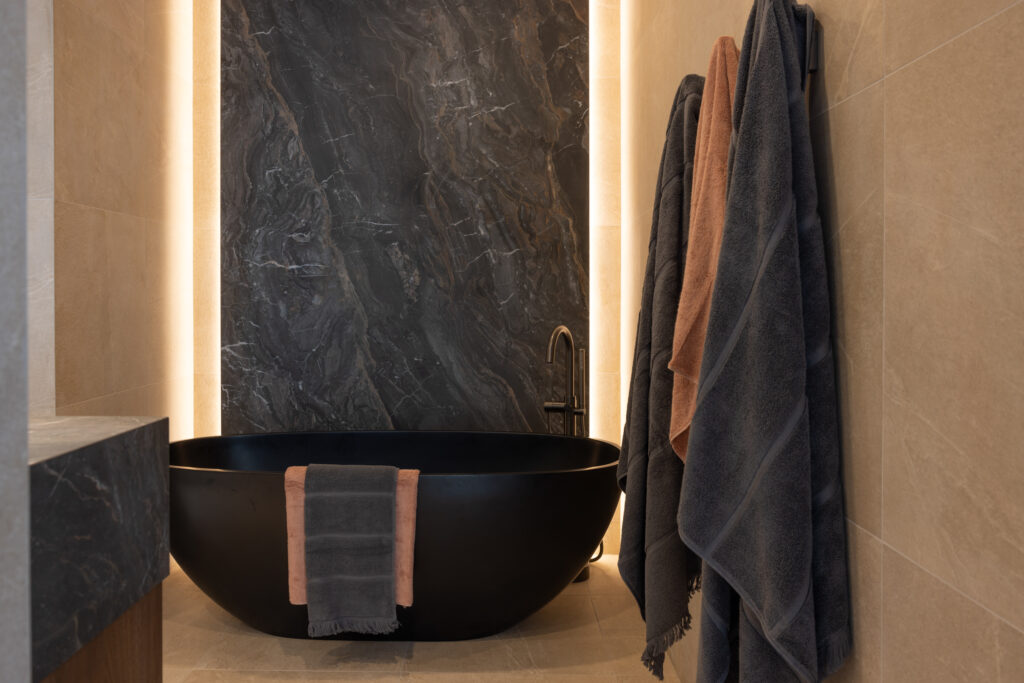 Interior deluxe bathroom with strip lighting around feature tile behind bath 
