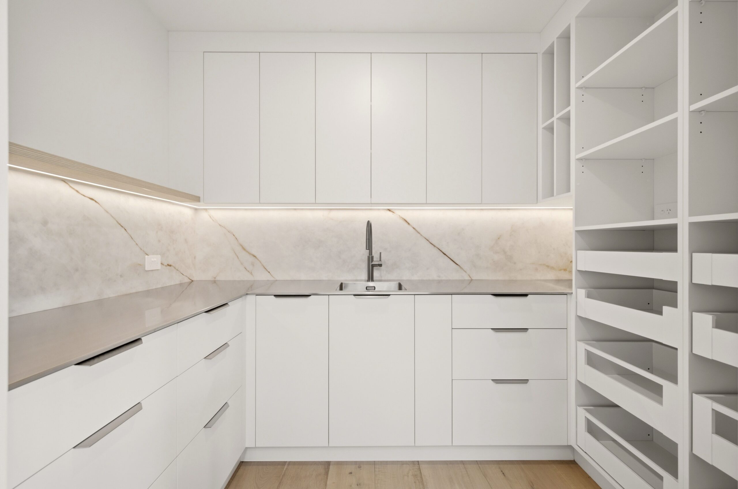 Wanaka plan, Hallmark Homes West Melton. Open-plan kitchen with light oak cabinetry, white upper cabinets, and a marble-look stone island.