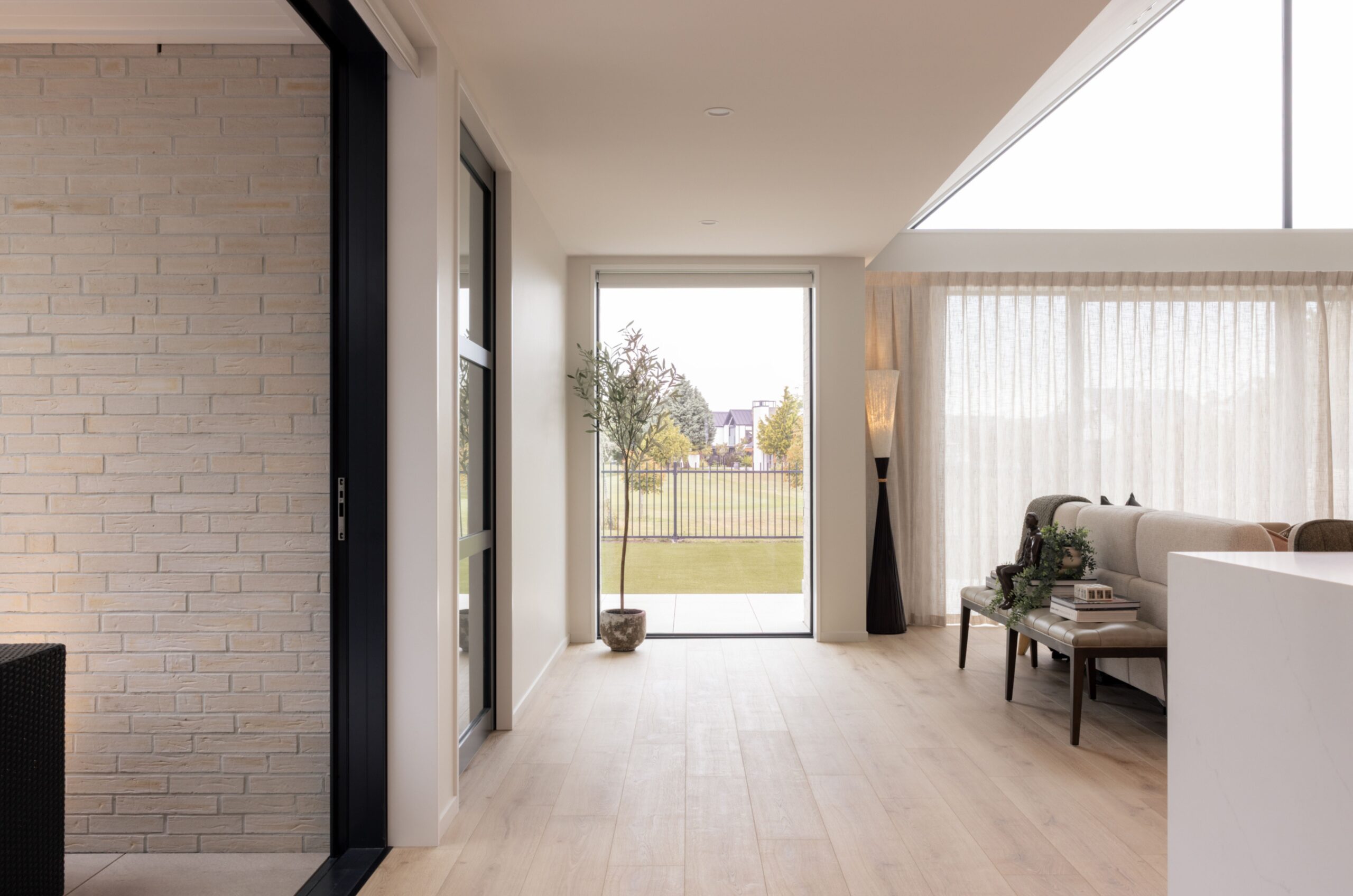 Hallway with feature brick wall, black-framed glass sliding door, timber flooring, and a golden retriever resting by the outdoor courtyard entrance. Hallmark Homes interior joinery, Marshlands, Christchurch.
