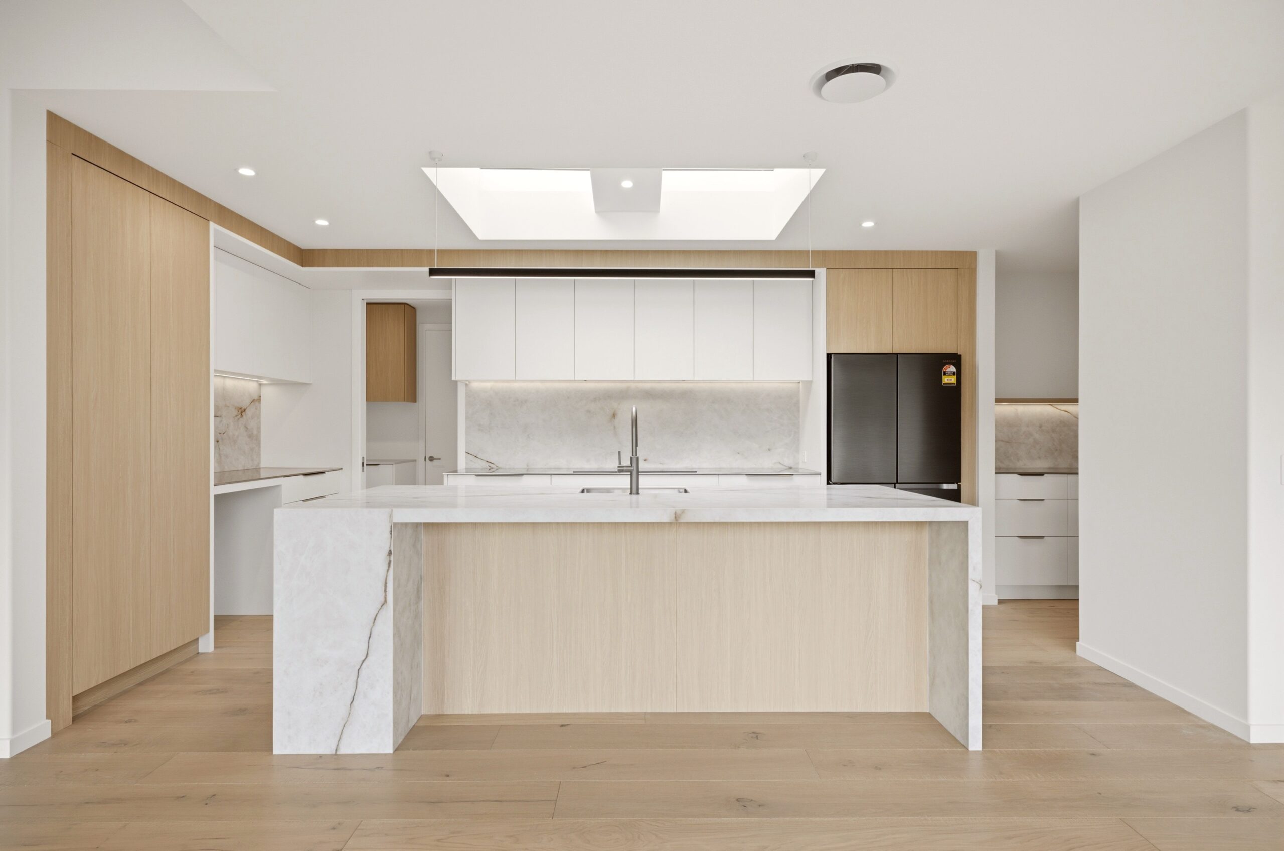 Wanaka plan, Hallmark Homes West Melton. Open-plan kitchen with light oak cabinetry, white upper cabinets, and a marble-look stone island.