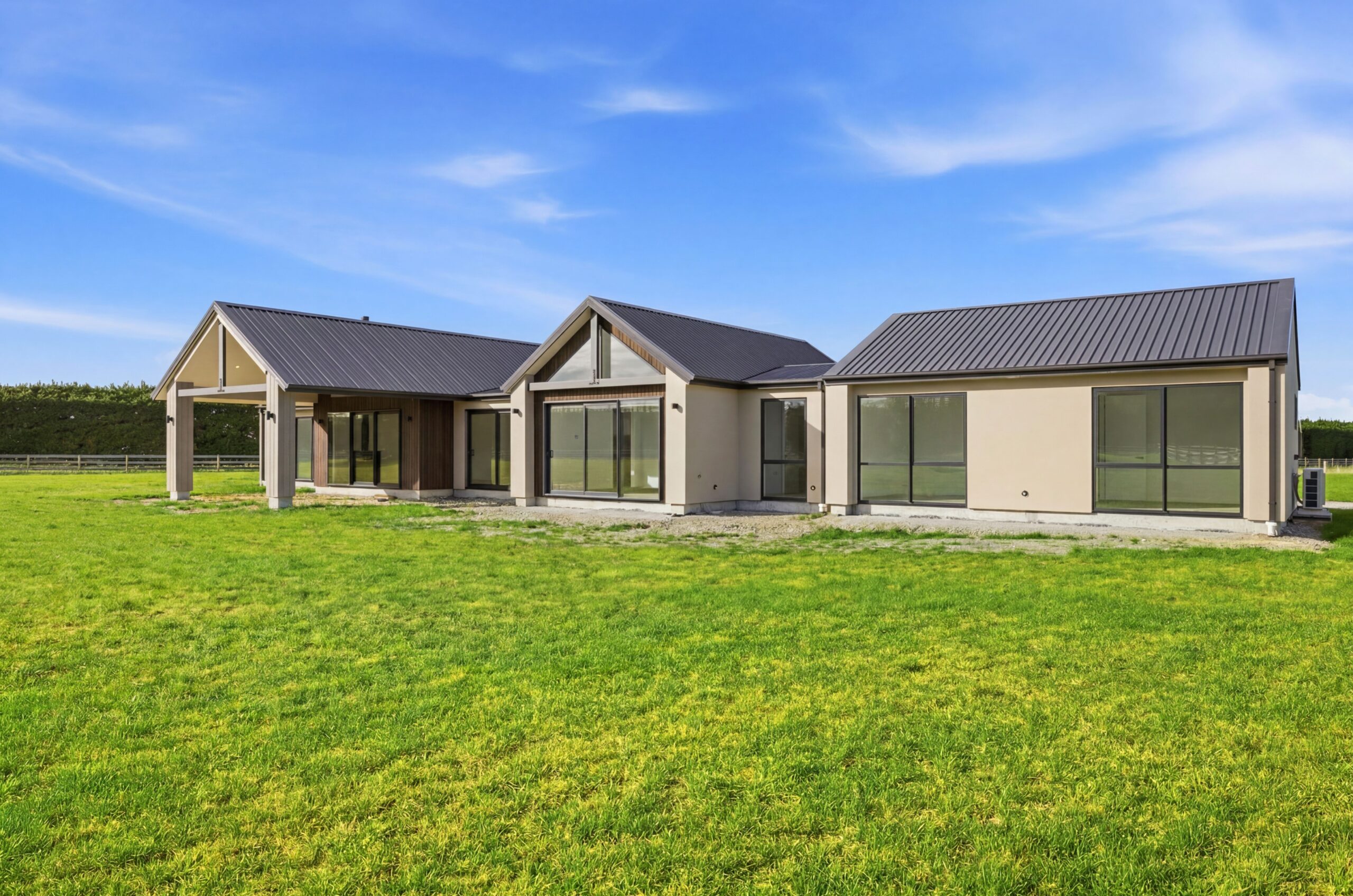 Wanaka plan, Hallmark Homes West Melton. Daytime view of the triple garage with dark panel doors and grey cladding.