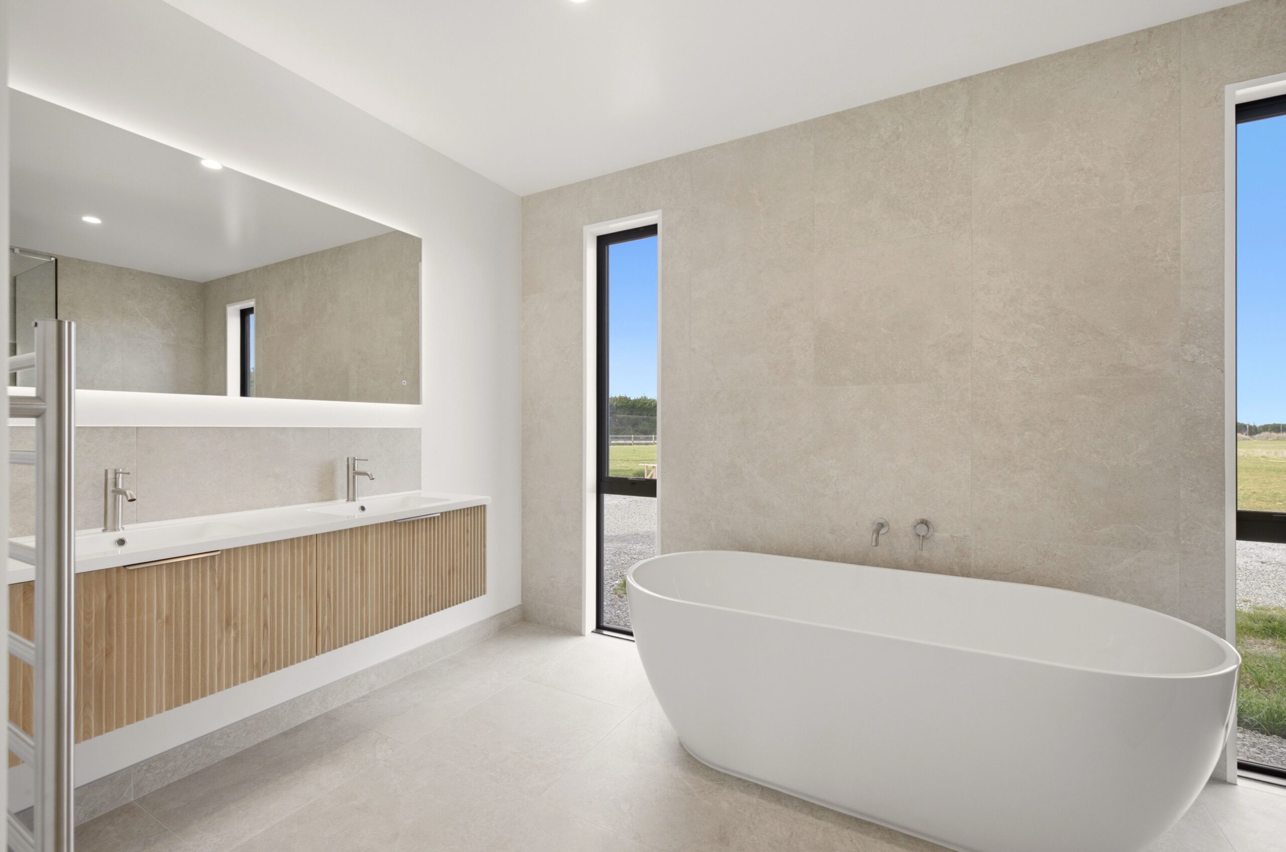 Wanaka plan, Hallmark Homes West Melton. Freestanding oval bathtub against a stone tiled wall with a tall window.